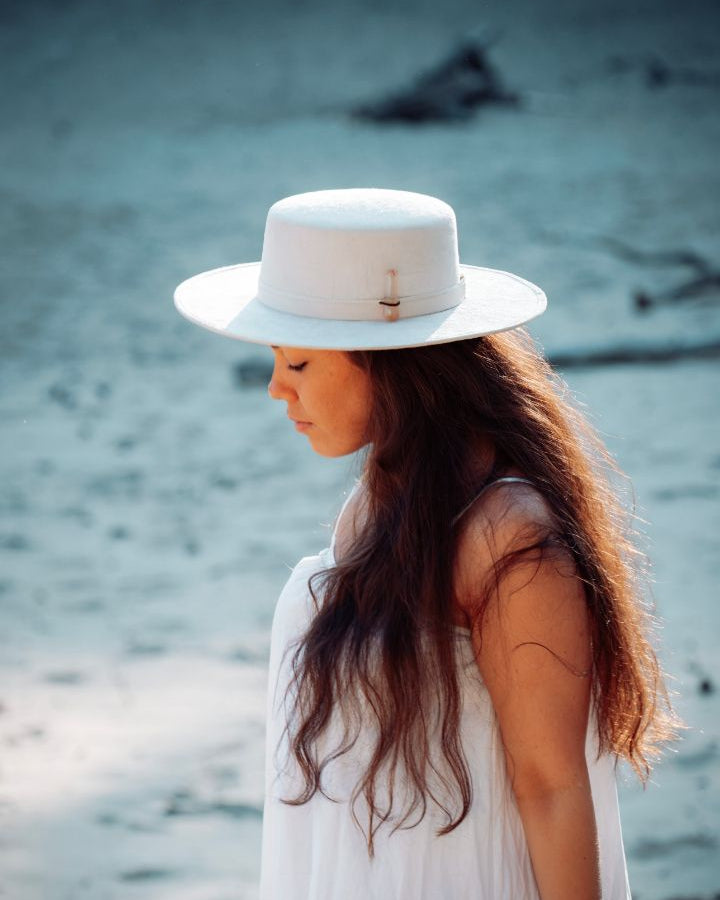 Witte flat top hoed voor dames met een hoedenband, gefotografeerd vanaf de zijkant.